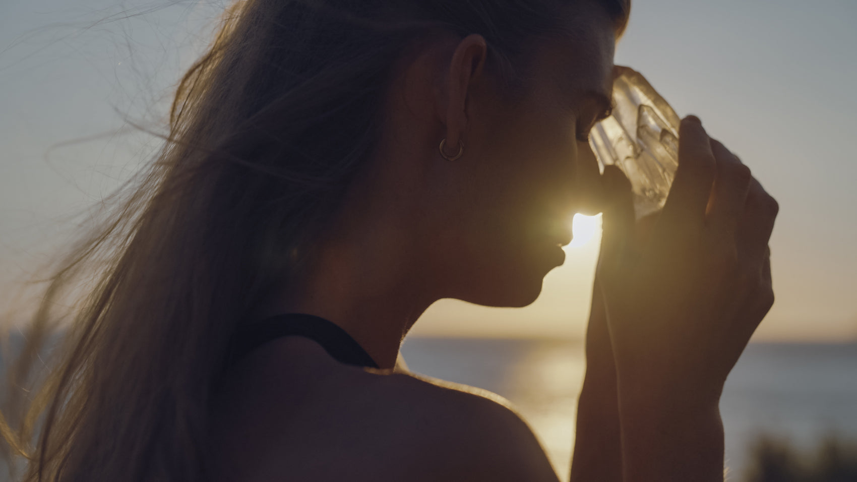 Silhouette of a woman meditating with a crystal at sunset, highlighting a peaceful and spiritual scene.