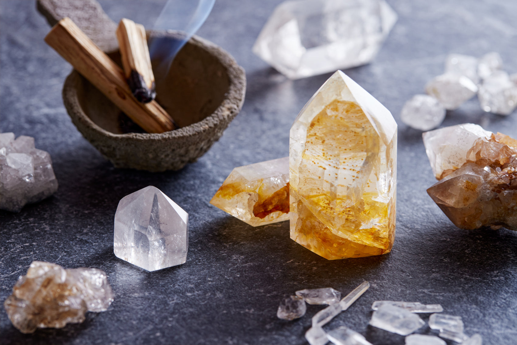 Citrine and clear quartz crystals arranged with a smoking incense bowl on a dark surface.