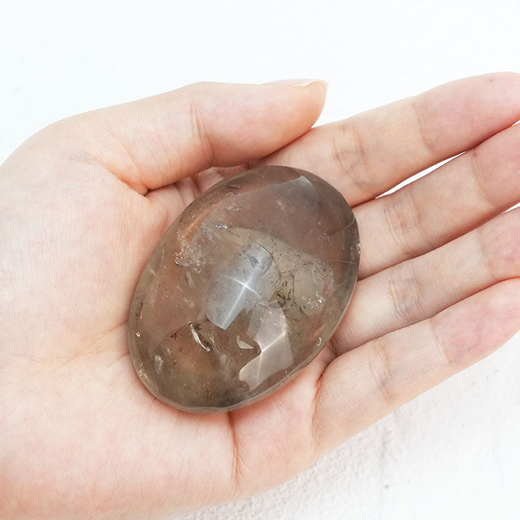 Smooth, round smoky quartz palm stone held in hand, symbolizing grounding and emotional stability.